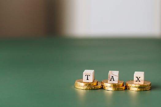 pexels-photo-6863186-6863186 Stacked gold coins with wooden blocks spelling 'TAX' on a green backdrop.